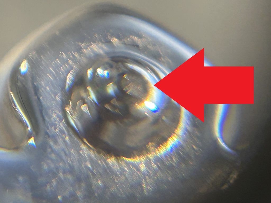 顕微鏡拡大写真、ピアス芯の折れた根元部分をマクロ撮影、赤い矢印で破断箇所を指示