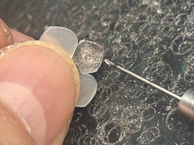 職人の指で押さえた半透明花弁パーツに小型ドリルで穴あけ加工している拡大写真