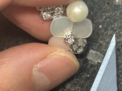 ピアス修理作業中、花弁パーツを取り付けたピアス本体を指で保持しながらカッターで微調整している拡大写真