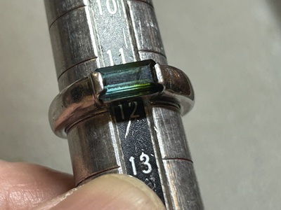 サイズ棒でグリーントルマリンリングの現在のサイズが12号弱であることを計測する様子