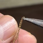 ピンセットの先端で極小のチェーンコマをつまんで溶接準備をする様子