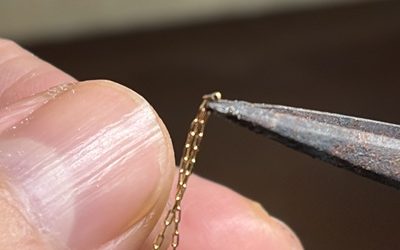 ピンセットの先端で極小のチェーンコマをつまんで溶接準備をする様子
